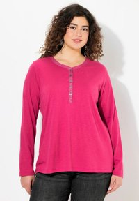 Langarmige pinke Bluse mit rundem Halsausschnitt, ausgestattet mit einer dekorativen Knopfleiste und strukturiertem Saum. Der Stoff wirkt weich und leicht.