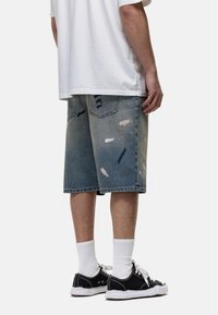 Lichtblauwe denimshorts met versleten plekken en rafelige randen, gecombineerd met zwarte sneakers en witte crew-sokken.