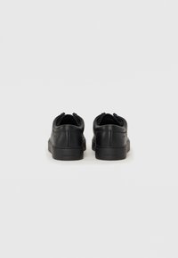 Sorte lærersneakers med en glat tekstur, rund tå og en lavprofil gummisål. Har subtil branding på hælen.