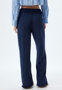 Navyblauwe wijde broek van zachte stof, met een rimpel-elastische tailleband. Gladde textuur, volledige lengte snit en minimale detailing.