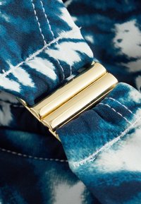Sinine ja valge lipsuvärviga kangas koos kuldse metallist pandlaga, millel on sile tekstuur ja kontrastne õmbluse detail.