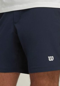Bañador azul marino hecho de material de secado rápido, con un logo blanco en el dobladillo izquierdo y una cinturilla elástica para mayor comodidad.
