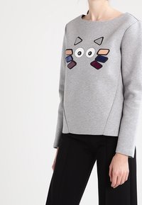 Sudadera gris con escote redondo y mangas largas, que presenta un diseño gráfico colorido y juguetón en la parte delantera con varias formas.
