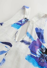 Blommönstrad klänning i lätt tyg. Krämfärgad botten med blå och lila blommor. Har en rundad halsringning och en knytning på baksidan.