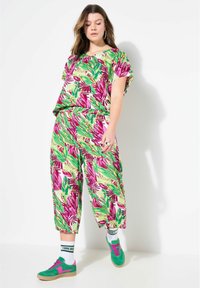 Conjunto de dos piezas floral con patrones de hojas verdes y rosas, top de corte relajado con mangas cortas, y pantalones sueltos y cortos. Combinado con zapatos verdes.