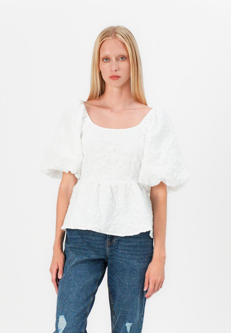 Top peplo bianco in tessuto testurizzato, scollatura quadrata e maniche a sbuffo, abbinato a jeans blu con strappi. Design semplice e casual.