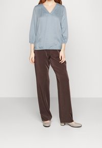 Blusa a cuadros en azul claro con escote en V y mangas tres cuartos; combinada con pantalones de pierna ancha en marrón oscuro; unas bailarinas grises completan el atuendo.