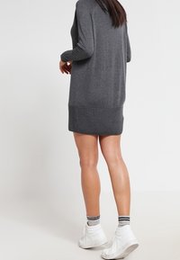 Graues Strickkleid mit geripptem Saum, langen Ärmeln und lockerer Passform, kombiniert mit weißen Turnschuhen und gestreiften Socken. Glatte Textur.