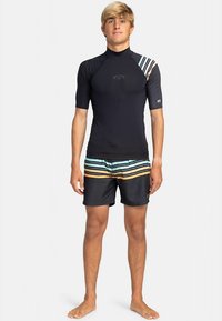 Svart rashguard med kort ärm och blåvita ränder; kombinerad med randiga badshorts i svart, teal och orange toner.