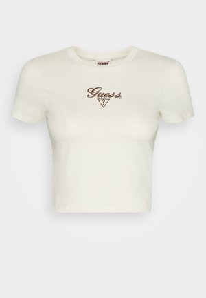 Kremowy krótki t-shirt z krótkim rękawem, okrągłym dekoltem, brązowym logo "Guess" i trójkątnym emblematem na środku klatki piersiowej.
