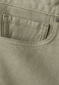 Gros plan sur un tissu en denim beige montrant une petite poche cousue à l'intérieur d'une plus grande poche avant de pantalon avec des coutures visibles et un rivet.