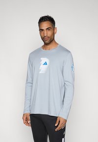 Light blue long-sleeve t-shirt made of soft fabric, featuring a white and blue graphic logo on the chest and a logo detail on the sleeve.