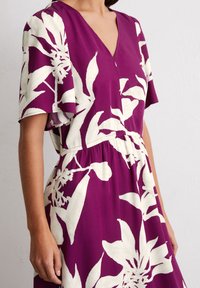 Lila Kleid mit weißen Blumenmustern, V-Ausschnitt, kurzen flatternden Ärmeln und einem elastischen Bund für eine entspannte Passform. Weicher, leichter Stoff.