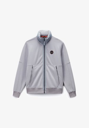 Chaqueta de cremallera gris claro, hecha de tejido suave, con un cuello alto, dos bolsillos frontales y un logo redondo en el lado izquierdo del pecho.