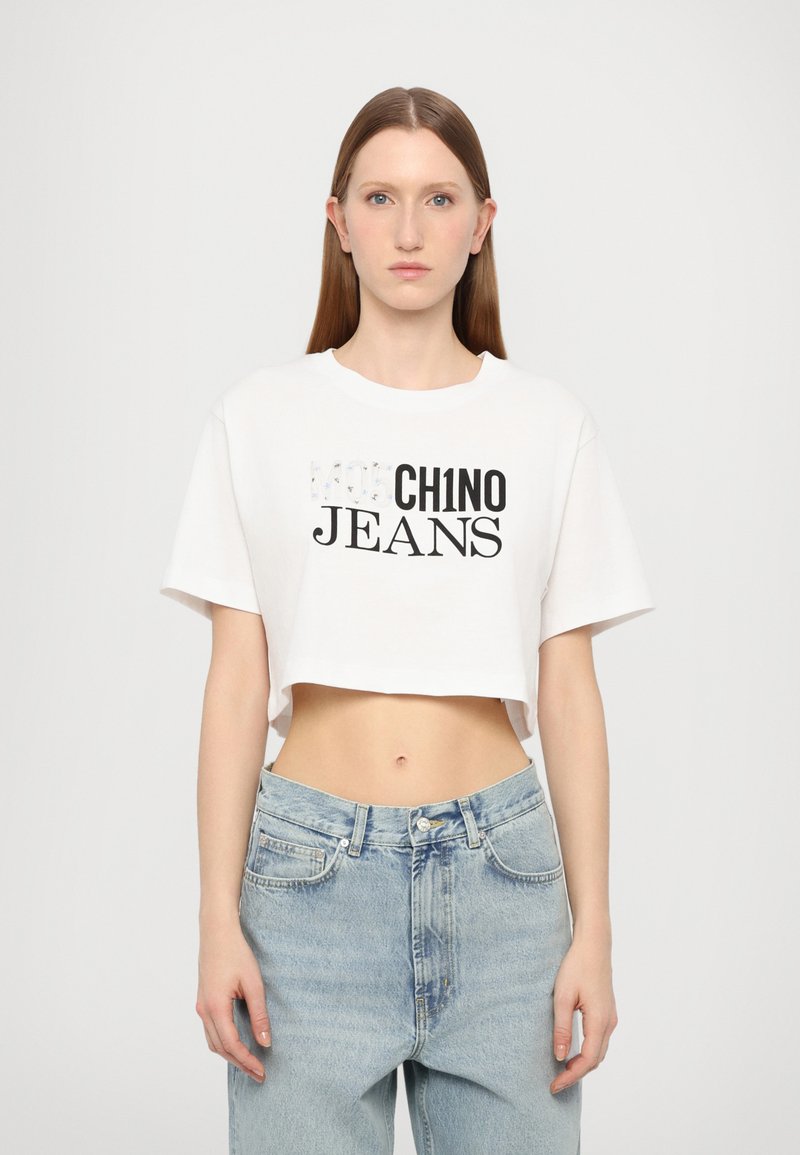 Balta trumpa marškinėliai su juodu ir sidabriniu tekstu "CHINO JEANS". Dėvima su šviesiai mėlynomis aukšta liemeniu džinsais. Lygi tekstūra.