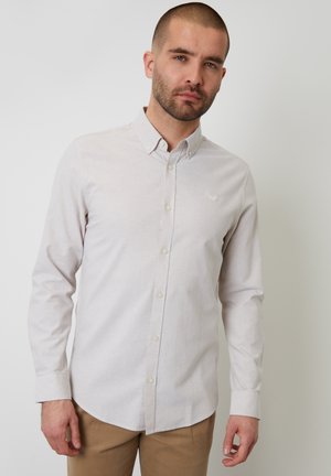 Camisa de botones beige claro con mangas largas y cuello, confeccionada con una tela suave con una textura sutil. Pequeño logo en el pecho.