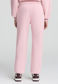 Pantaloni della tuta rosa chiaro realizzati in tessuto morbido, con una vestibilità comoda e vita elastica. Texture liscia senza motivi o dettagli visibili.