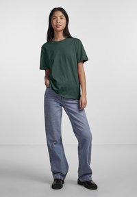 Camiseta de algodón verde oscuro con cuello redondo y mangas cortas, combinada con unos vaqueros sueltos de color azul claro y zapatos negros.