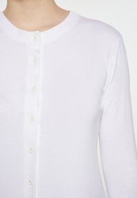 Witte gebreide cardigan met een ronde hals, lange mouwen en een sluiting met zes knopen aan de voorkant. Glad textuur, slim-fit ontwerp en geen zichtbare patronen.