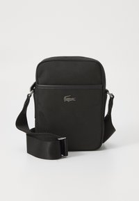 Black fabric crossbody bag with a textured surface, branded logo in silver, adjustable strap, and a simple, rectangular design.