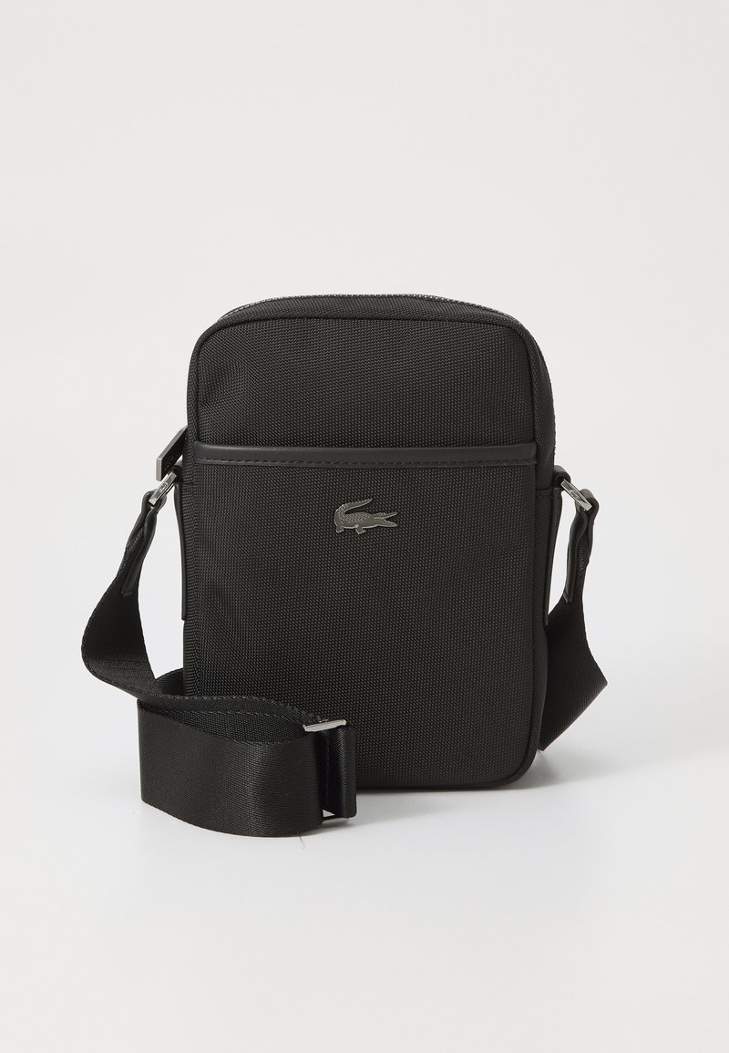 Black fabric crossbody bag with a textured surface, branded logo in silver, adjustable strap, and a simple, rectangular design.
