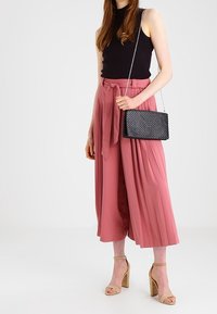 Top nero senza maniche, pantaloni ampi plissettati rosa con un nodo in vita e una borsa a tracolla nera intrecciata. Sandali con tacco alto beige.