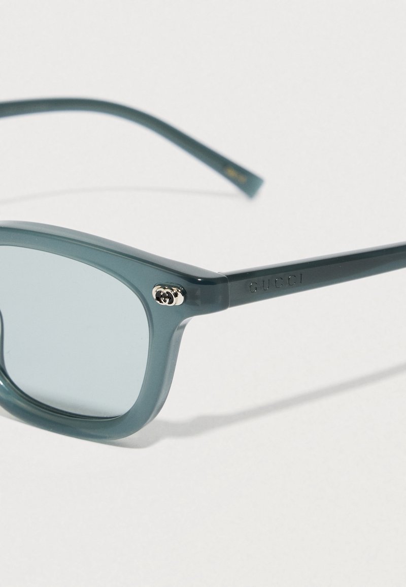 Blue-tinted rectangular Gucci sunglasses with thin plastic frames and silver double-G logo detail on the temple.
