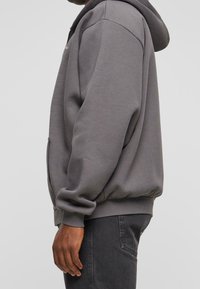 Sudadera gris con cierre y capucha ajustable, puños con canalé y cintura con canalé. Tejido suave de mezcla de algodón, bolsillos laterales y un diseño con mínima identificación.