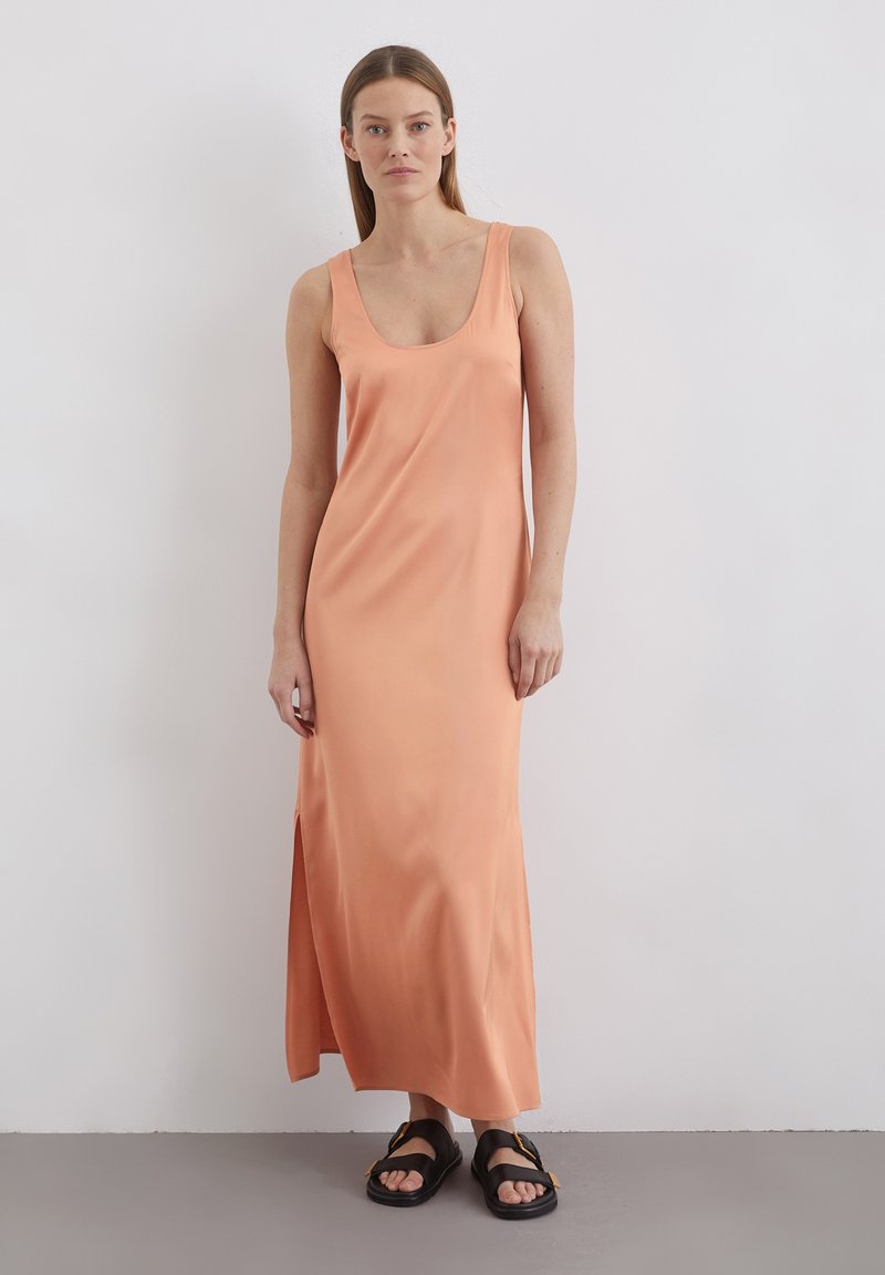 Robe longue sans manches en tissu pêche doux avec un col rond et une fente sur le côté, associée à des sandales noires au design de brides.