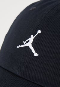 Sort baseball cap med tekstureret overflade, prydet med et hvidt broderet Jumpman-logo på fronten.