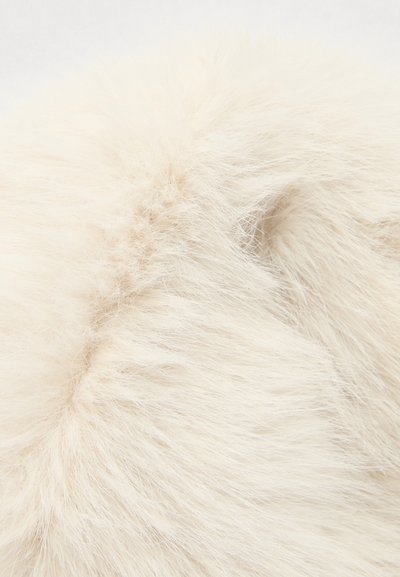 Gestructureerde crème-kleurige kunstbont met lange, zachte draden, die een dikke en pluizige uitstraling hebben. De naden zijn subtiel zichtbaar.