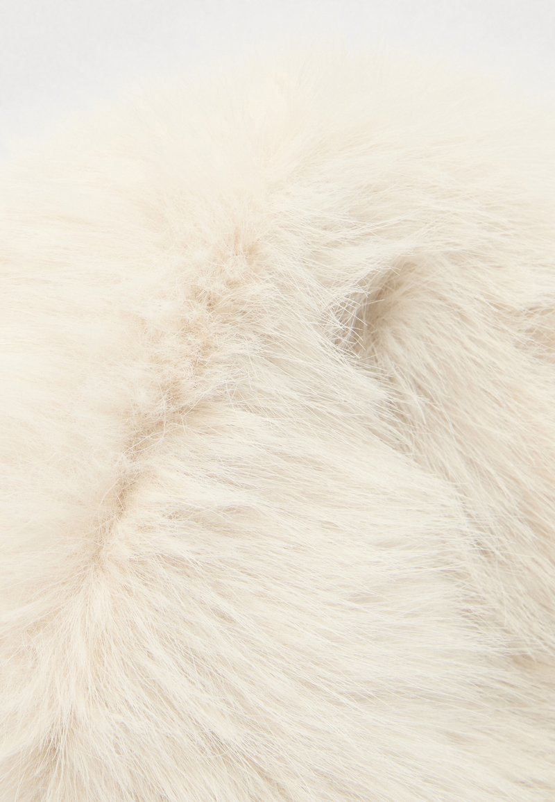 Tekstureret flødefarvet kunstpels med lange, bløde strå, der viser et tykt og fluffy udseende. Sømme er let synlige.