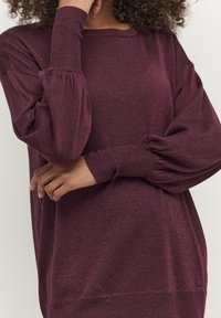 Bordeaux pullover trui van fonkelend breimateriaal. Heeft losse mouwen met ribgebreide boorden en een brede halslijn. Zachte textuur.