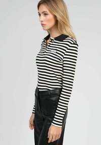 Polo à manches longues rayé noir et blanc avec un col noir et une petite étiquette "1985". Associé à un pantalon en cuir taille haute.