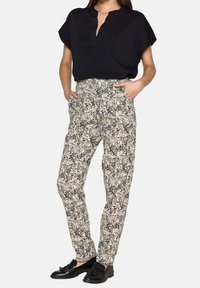 Zwart T-shirt met korte mouwen, losse pasvorm; gemusterde crèmekleurige broek met zwart bloemenpatroon; platte zwarte schoenen; zakken op de broek.