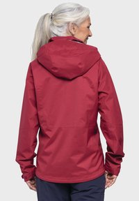 Giacca rossa impermeabile con cappuccio. Presenta una texture liscia e un design aderente, cuciture visibili e polsini regolabili. Vista posteriore mostrata.