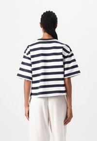 Top de rayas de algodón blanco y navy de manga corta, con un ajuste relajado y cuello redondo; detalles de costura visibles en el dobladillo y las mangas.