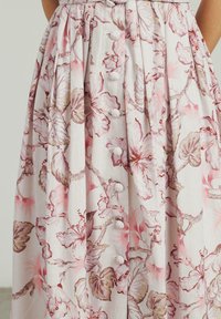 Gonna midi floreale in tessuto beige chiaro con motivi di fiori rosa e marroni. Decorata con bottoni decorativi e morbide pieghe.