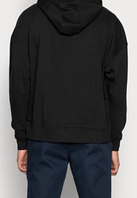 Svart huvtröja med avslappnad passform, ribbade mudd och fåll samt en mjuk textur. Matchad med marinblå byxor.