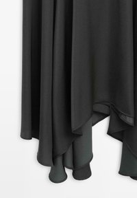 Tessuto grigio scuro con orli curvi stratificati e irregolari che pendono davanti a uno sfondo bianco.