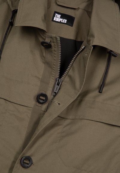 Giacca khaki con bottoni neri, zip parzialmente aperta, cordini regolabili e etichetta "THE KOOPLES" all'interno del collo.