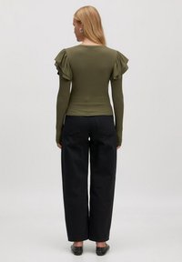 Olijfgroene geribbelde langemouwen top met gerimpelde schouderaccenten, gecombineerd met hoge taille zwarte wijde pantalons en zwarte schoenen.