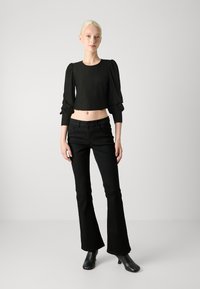 Top negro corto con mangas abullonadas y patrón texturizado, combinado con jeans negros acampanados y botas de tobillo. Tela suave, silueta ajustada.