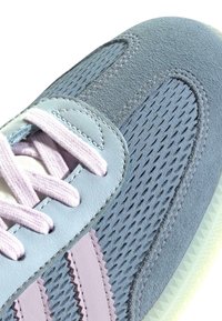 Plavi tenisice s svijetloružičastim prugama i vezicama, od mrežaste i nubuk teksture, te prozirnom obrazcu potplata vidljivim na bijeloj pozadini.