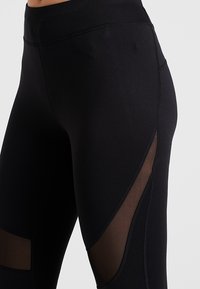 Czarne legginsy z wysokim stanem, z siateczkowymi panelami po bokach. Gładka tekstura z wzmocnionymi detalami szwów.