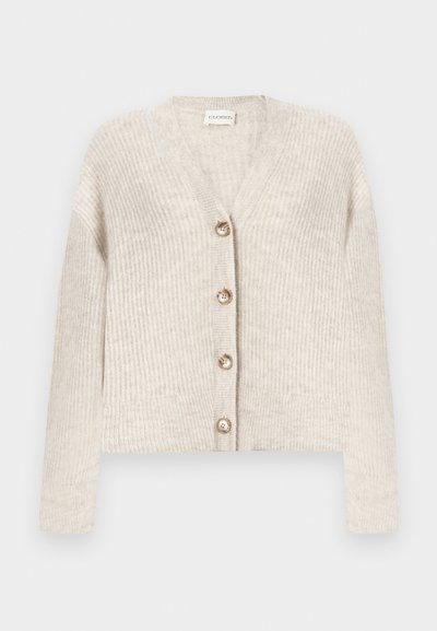 Μπεζ ριγωτή πλεκτή ζακέτα με V-λαιμόκοψη, μακριά μανίκια και τέσσερα κουμπιά στο μπροστινό μέρος, τοποθετημένη επίπεδα σε λευκό φόντο.