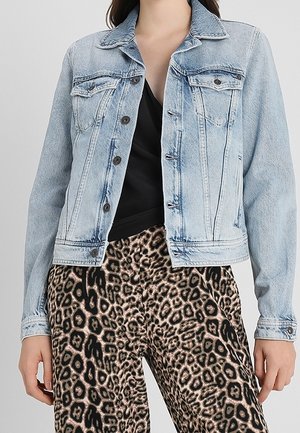 Lyseblå denimjakke knappet over sort top, kombineret med højttaljede leopardprintbukser, båret af en stående person.