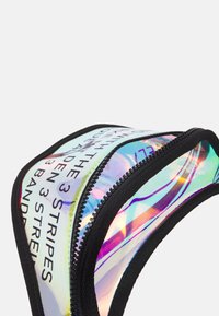 Holografická kapsa na zip s černými detaily, vybavená výraznou typografií a hladkým, reflexním povrchem. Zakřivený design zdůrazňuje tvar.