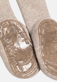 Calze di un colore beige con suola in grip traslucida e lucida. Il tessuto lavorato a maglia presenta una finitura liscia con dettagli a costine nella parte superiore.