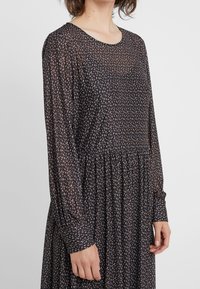 Robe noire à manches longues avec un col rond, présentant un motif de feuilles roses et blanches dispersées, une taille plissée et des poignets de manches froncés.